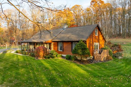 Log home exterior with a covered front porch and side wood deck framed by autumn trees
