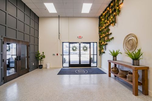 Lobby with dark paneled accent wall, glass entry doors, hanging greenery, and terrazzo flooring