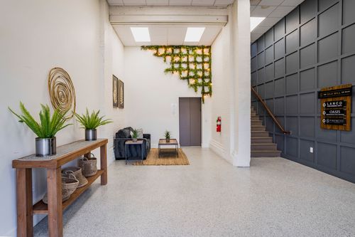 Lobby with hanging greenery installation, dark paneled staircase wall, and a leather loveseat