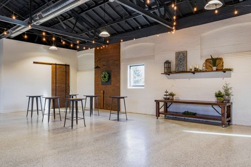 Event space with string lighting, a wood sliding barn door, and standing cocktail tables