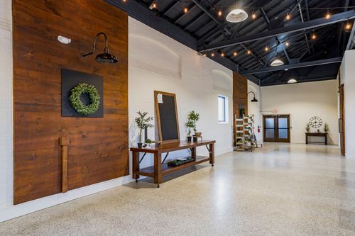 Event hallway with a wood accent wall, wreath, mirror, and arched brick windows under string lights
