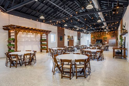 Banquet hall with a wood pergola arbor, hanging greenery, and round tables set for an event under string lights
