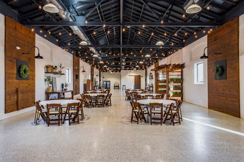 Banquet hall with string lights overhead and round tables set with white linens and wood chairs