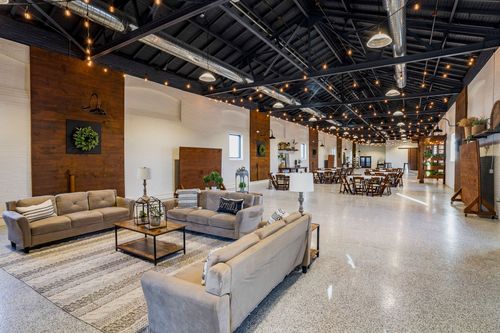 Lounge seating with sofas and an area rug beside dining tables in a long event hall