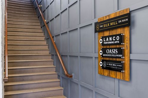 Wood staircase with dark paneled wall and tenant directory signage in a converted mill lobby