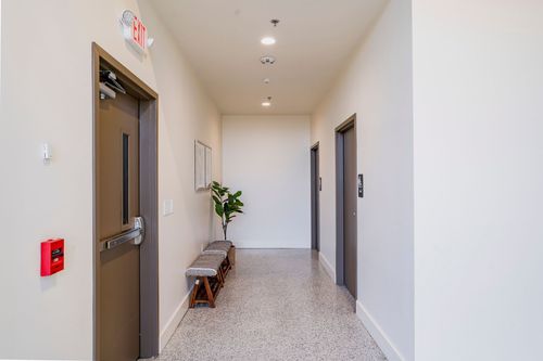 Hallway with closet doors, a bench and plant, leading to an arched brick window
