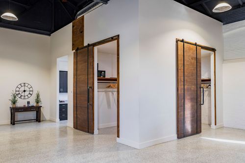 Two dressing rooms with open sliding barn doors revealing hanging rods and wood shelving