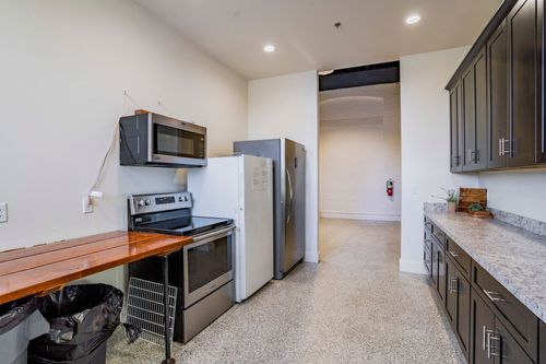 Catering kitchen with dark cabinets and stainless appliances opening to a hallway lounge