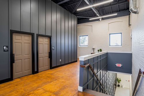 Hallway with restroom doors, dark paneling, wood flooring, and a reception counter near arched brick windows