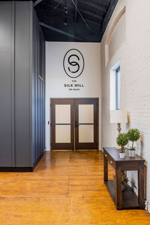 Lobby entry with a circular logo on white plaster, wood double doors, and a console table beside exposed brick