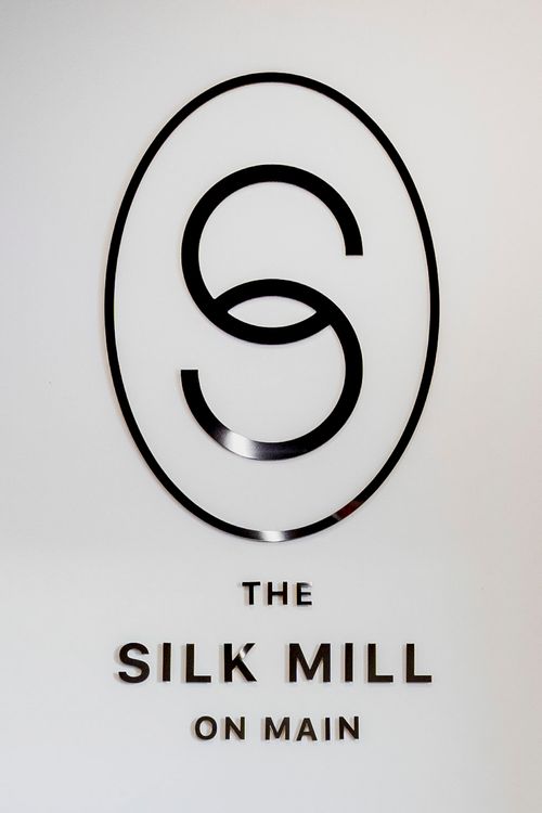Close-up of The Silk Mill on Main circular logo mounted on a white plaster wall