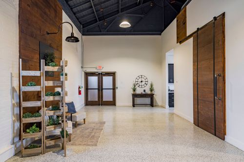 Open event hallway with a wood sliding barn door, gooseneck lighting, and a wall clock