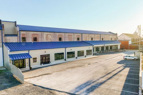Aerial view of a converted brick mill building with a blue standing-seam roof and storefront awnings
