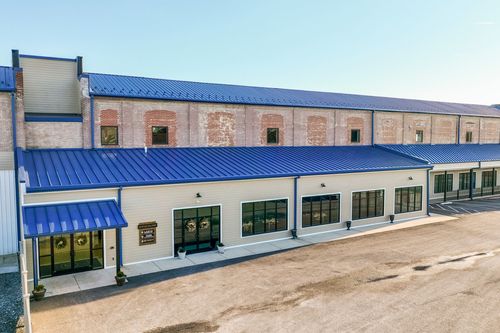Aerial view of a renovated brick mill with blue metal roofing and glass storefront entrances