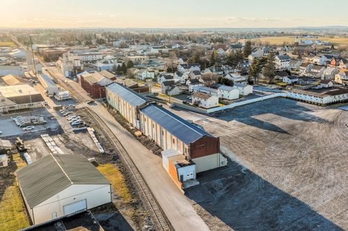 Aerial dusk view of an elongated mill building alongside railroad tracks in a small town