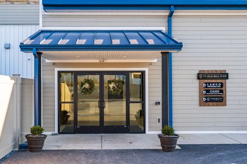 Close-up of a mill building's blue standing-seam entrance awning with glass doors and wreaths