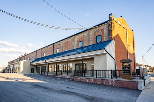 Street-level view of a mill building corner with an orange brick tower and blue roof trim