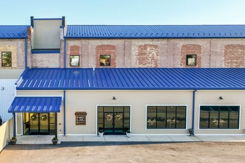 Converted mill building with a blue standing-seam roof, brick and tan facade, and an awning-covered entrance