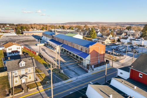 Aerial dusk view of a renovated brick mill complex with blue metal roofing beside a small town