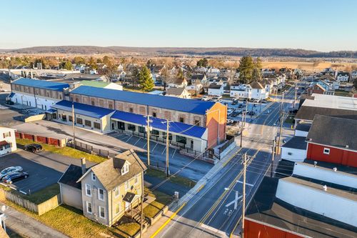 Aerial view of a long brick mill building with blue roof and orange accent tower near a railroad crossing