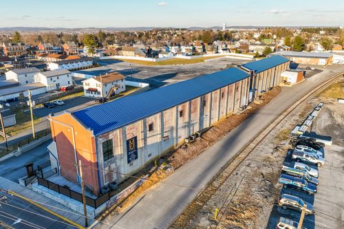 Aerial view along a mill building's blue roofline with an orange brick tower and rail line alongside
