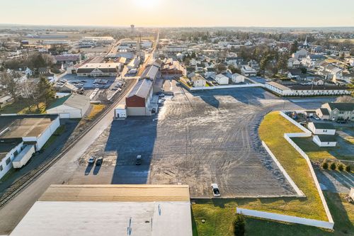 Aerial dusk view of a expansive dirt lot bordered by a landscaped retaining wall near the mill building