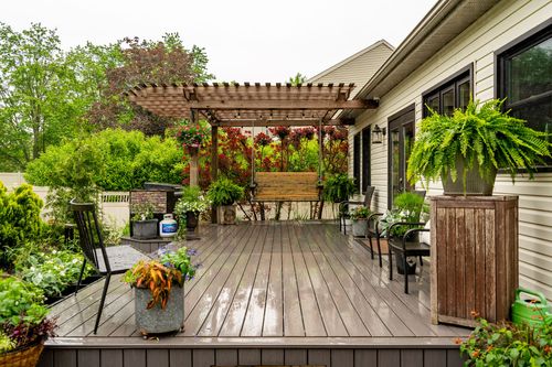 Back deck with a wood pergola, potted ferns, and a swing surrounded by climbing florals