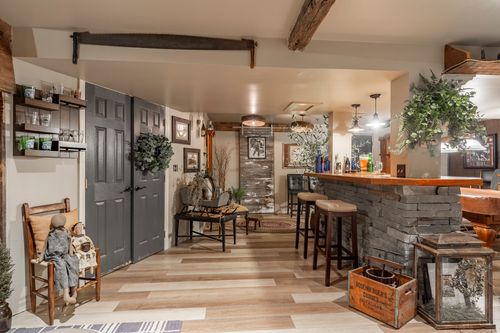 Basement rec room with charcoal double doors, a wreath, wood beam and a stone bar beyond