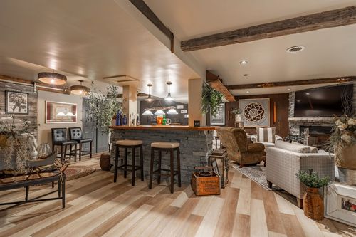 Basement bar and lounge with stone counter, wood beams and a stone fireplace with mounted TV