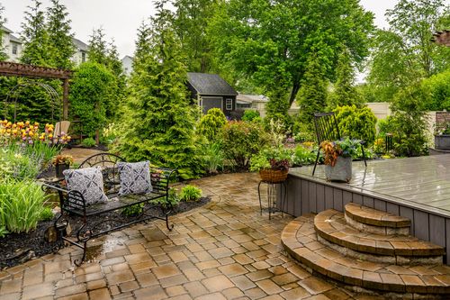 Stone paver patio with a wrought iron bench, blooming hydrangeas, and steps up to a deck