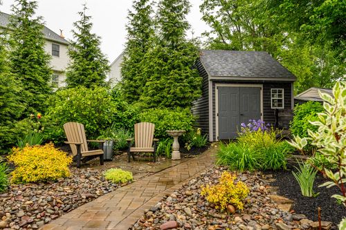 Backyard seating nook with adirondack chairs, a birdbath, and a dark-shingled garden shed
