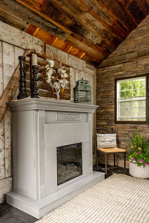 Rustic white fireplace with a weathered wood accent wall and stacked stone corner in a converted studio