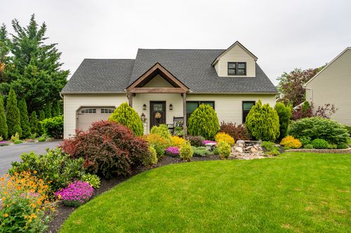 Cream siding home with gray roof and colorful landscaped garden beds along the front lawn