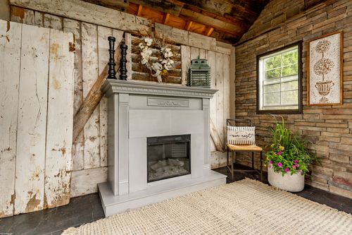 White painted fireplace against a distressed wood wall with a woven chair and potted florals nearby