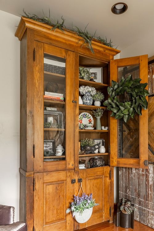 Close view of a wood hutch styled with dishware, greenery, and a hanging wreath on the open door