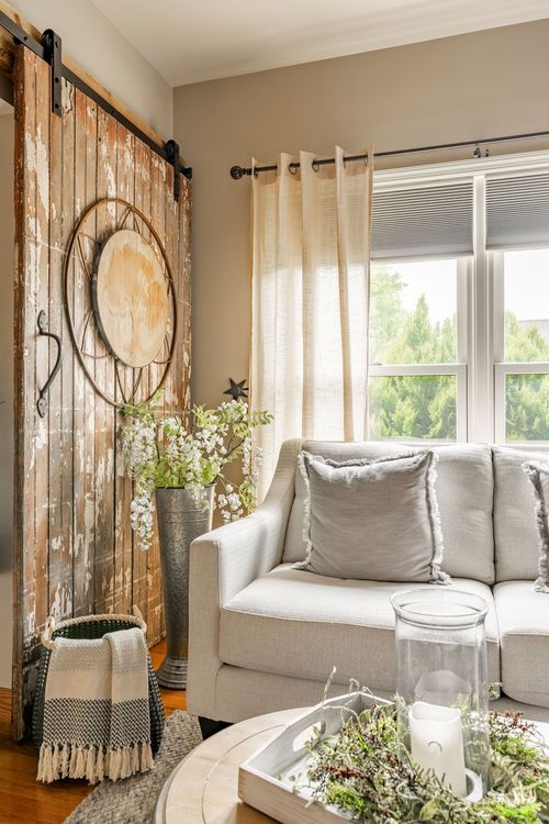 Rustic sliding barn door with a round mirror accent beside a cream sofa near a window