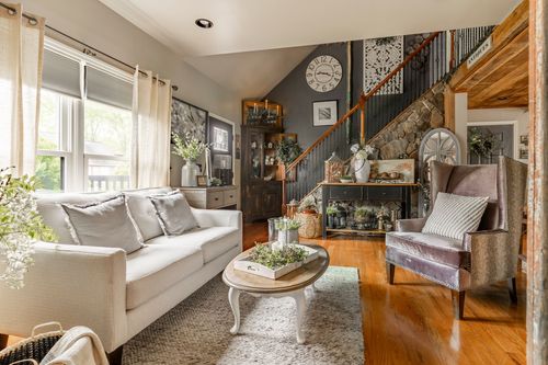 Living room with a cream sofa, wingback chair, wood staircase, and stone accent wall
