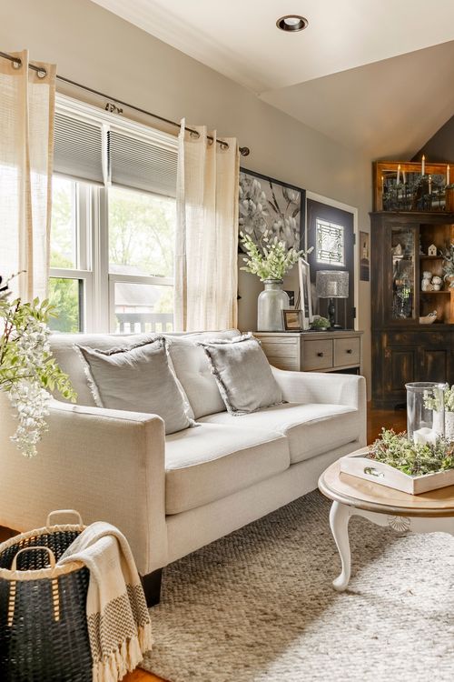 Living room seating with a linen sofa, sheer curtains, and a dark farmhouse hutch