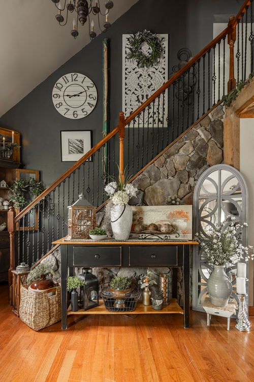 Entryway with a wood staircase over a stone base, oversized wall clock, and a styled console table