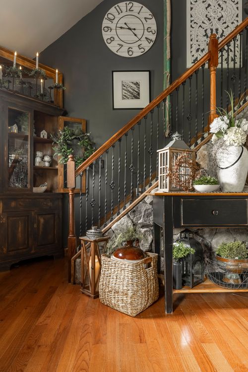 Staircase landing with a large wall clock, dark hutch, and console table styled with lanterns