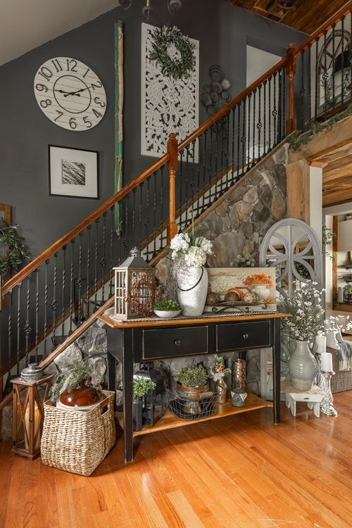 Entryway with a wood staircase, wall clock, and a black console table styled with lanterns and florals