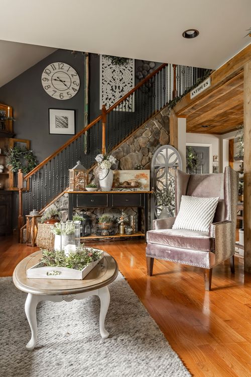 Living room with a dark accent wall, staircase, wingback chair, and round farmhouse coffee table