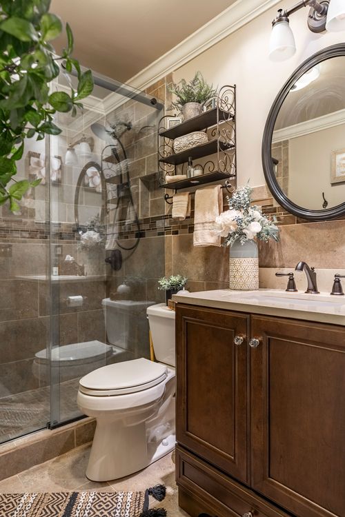 Bathroom with a glass shower, round mirror, dark wood vanity, and a fresh floral arrangement
