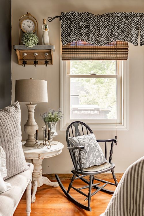 Corner nook with a wall shelf, table lamp, and a black windsor rocking chair by a curtained window