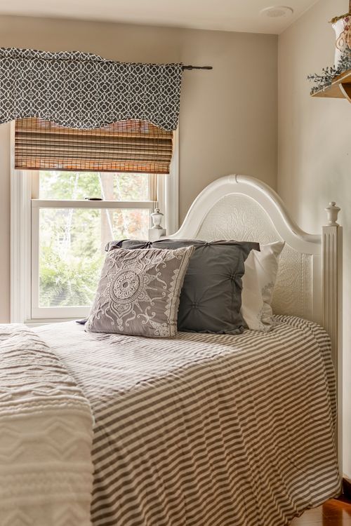 Close view of a white headboard bed with striped bedding and layered gray pillows