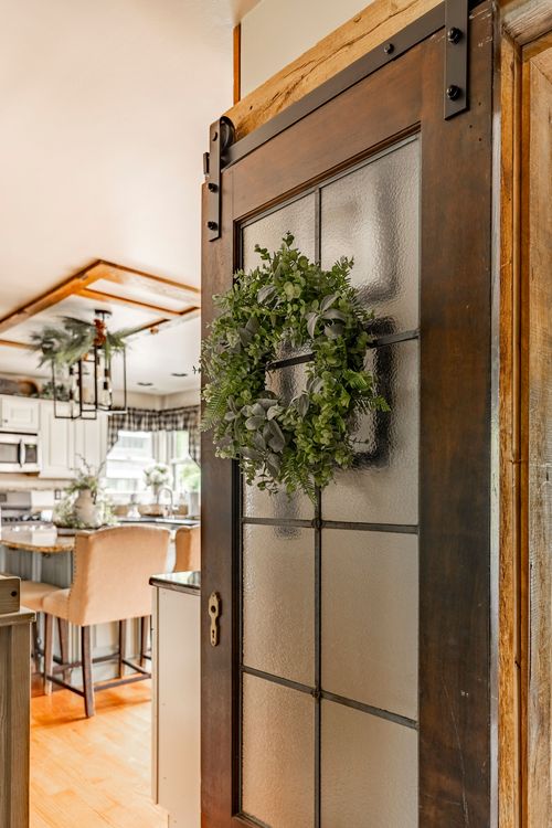 Sliding barn door with frosted glass panes and a greenery wreath opening into a farmhouse kitchen