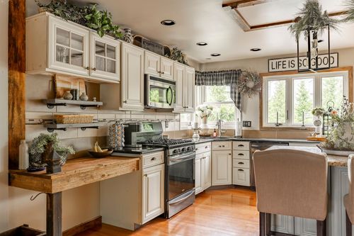Farmhouse kitchen with white cabinetry, greenery accents, and a stainless range beneath a wood beam ceiling