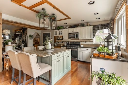 Kitchen island with a wood pendant beam feature, sage green cabinetry, and upholstered barstools