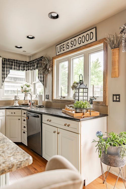 Kitchen with a Life Is So Good sign above the window, black plaid valance, and dark soapstone counters