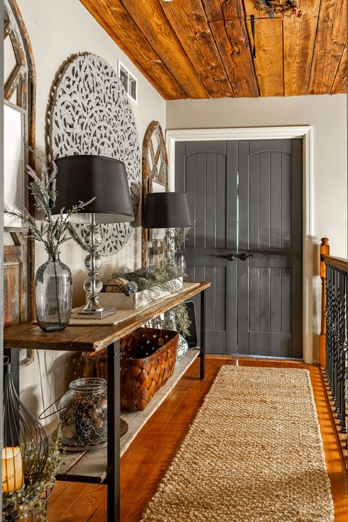 Hallway with a console table, arched mirrors, dark double doors, and a jute runner rug